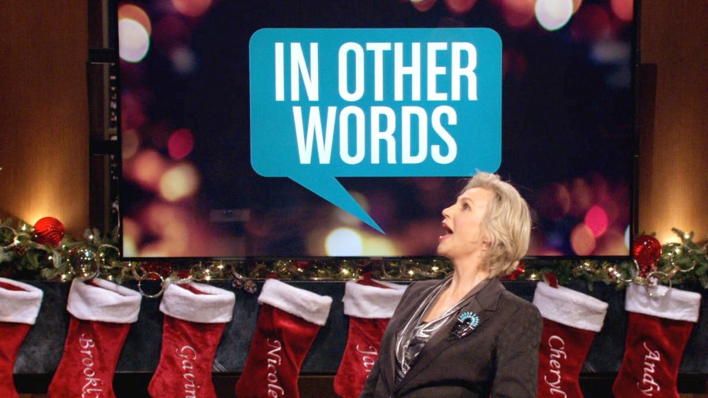 Jane Lynch in front of the logo for In Other Words
